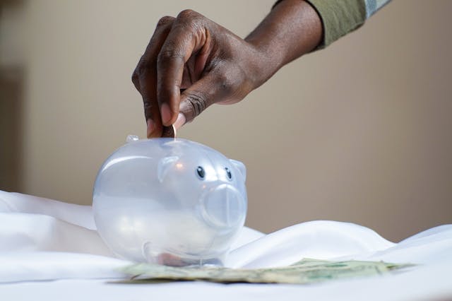person placing coins into a clear piggy bank