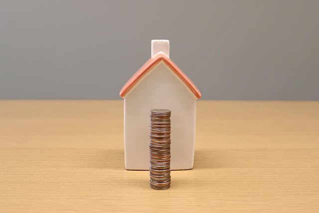 a home figurine with a stack of coins in front of it