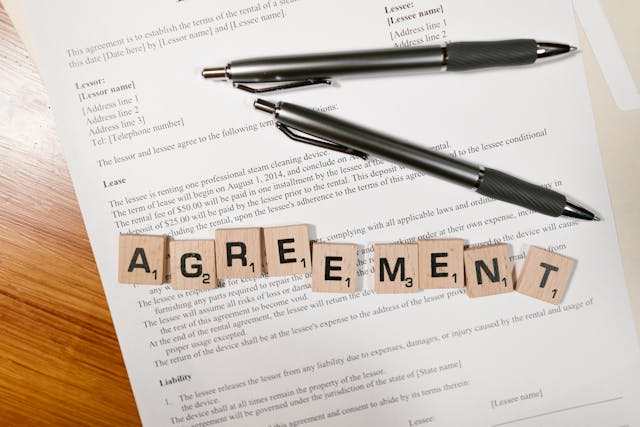 a lease with two pens on top and scrabble tiles spelling out the word "agreement"